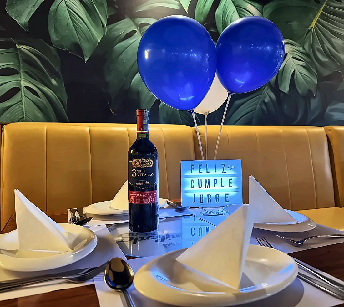 Mesa decorada con globos, vino y letrero de feliz cumpleaños