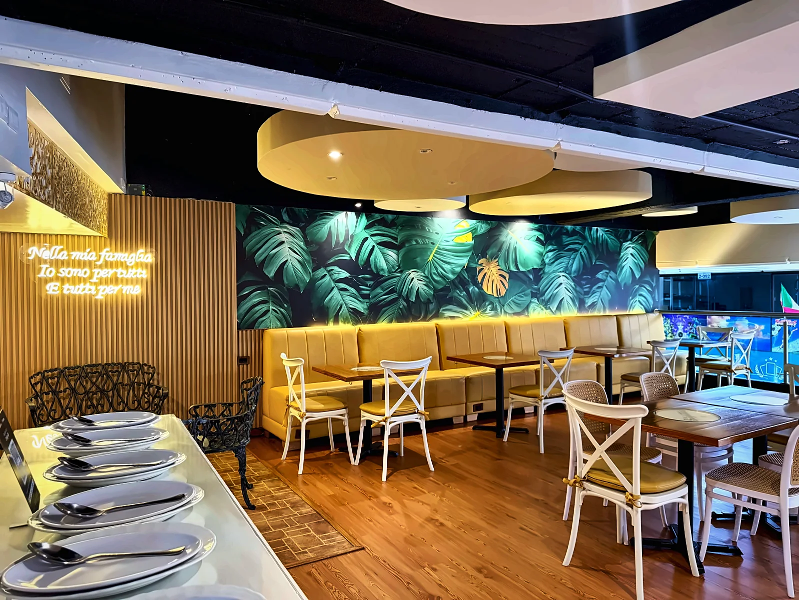 Salón de La Spaghettata con mural de hojas tropicales y sillas blancas